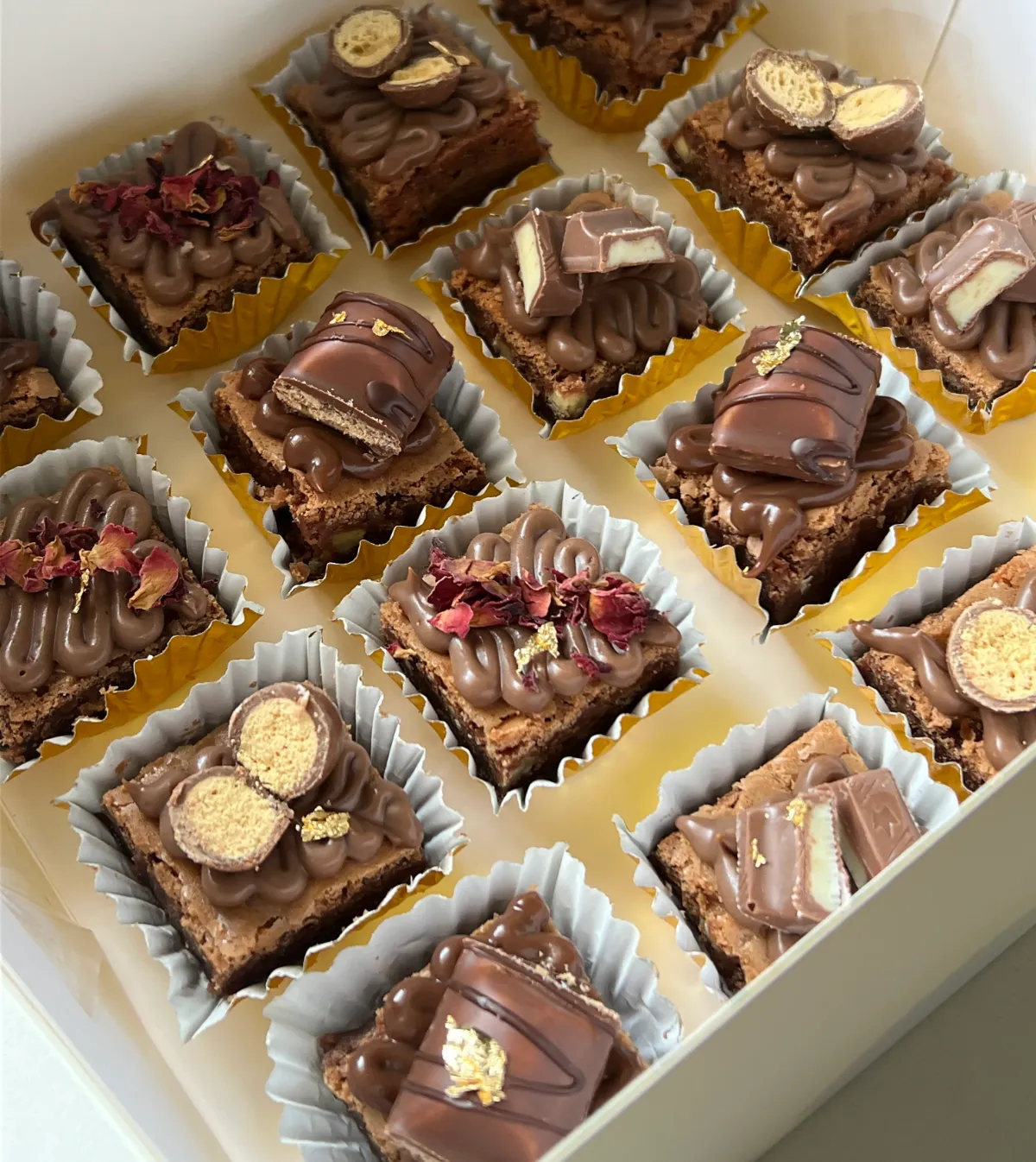 A box of gourmet brownie squares topped with chocolate, Kinder Bueno, dried rose petals and gold leaf