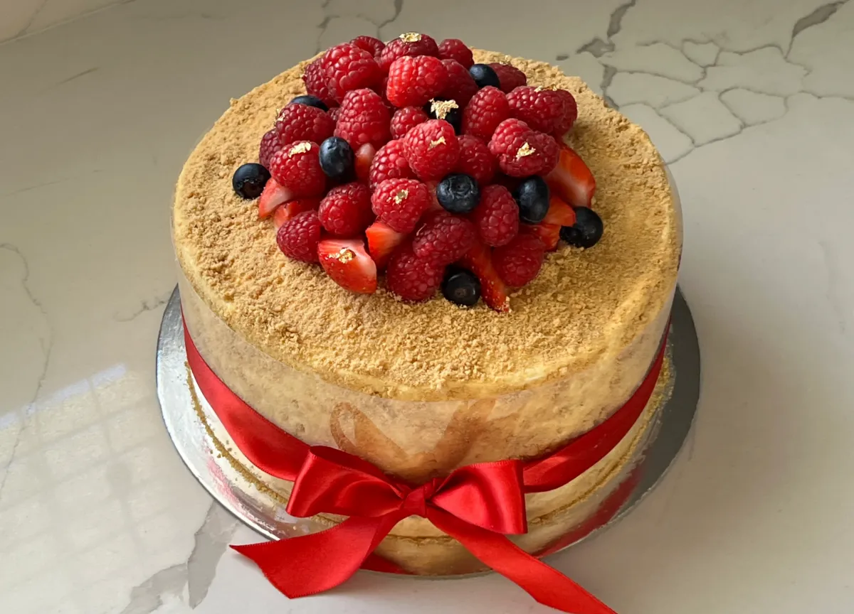 A honey crumb layer cake topped with fresh raspberries, blueberries, strawberries and edible gold leaf, finished with a red ribbon